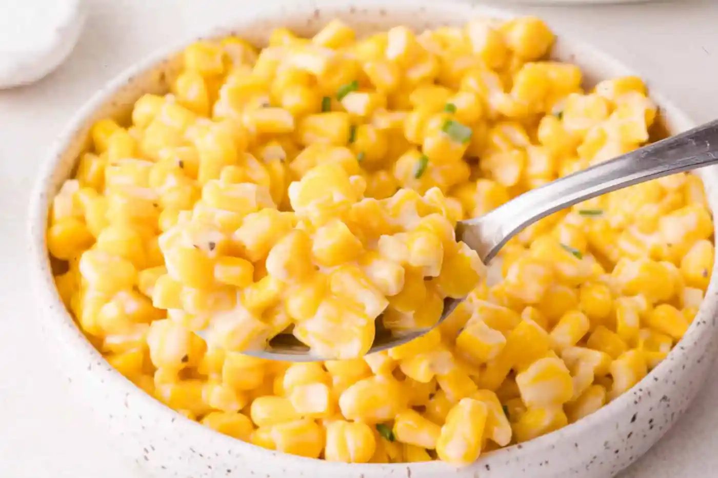 A close-up of a spoonful of creamy honey butter corn being lifted from a bowl filled with creamed corn.