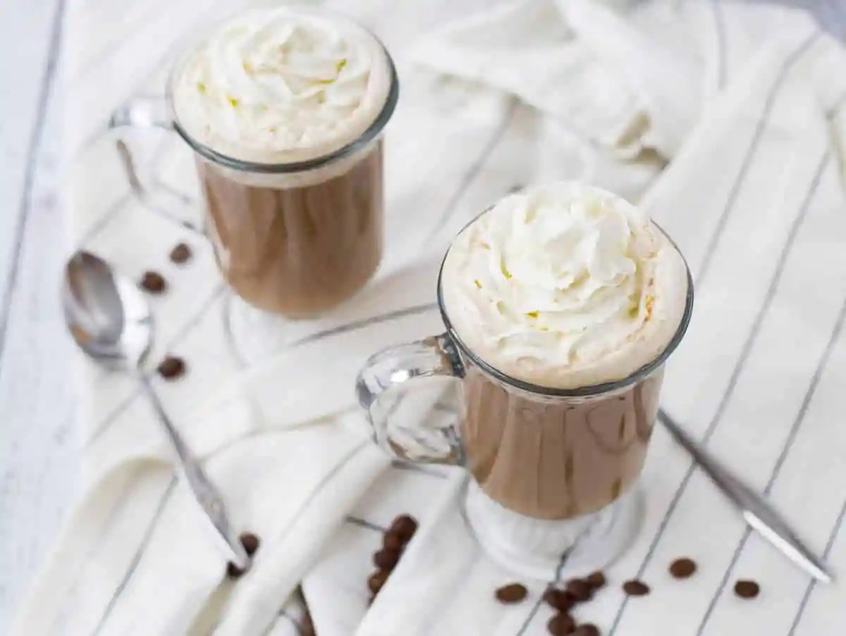 Overhead of two mugs of white russian on white striped cloth.