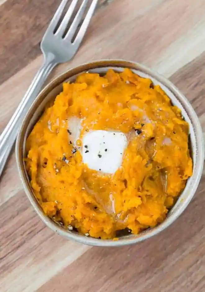 Overhead of mashed squash in small bowl with pat of butter melting in it and sprinkled with black pepper.
