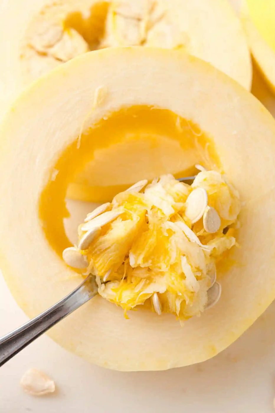 Seeds being removed from spaghetti squash ring with a spoon.