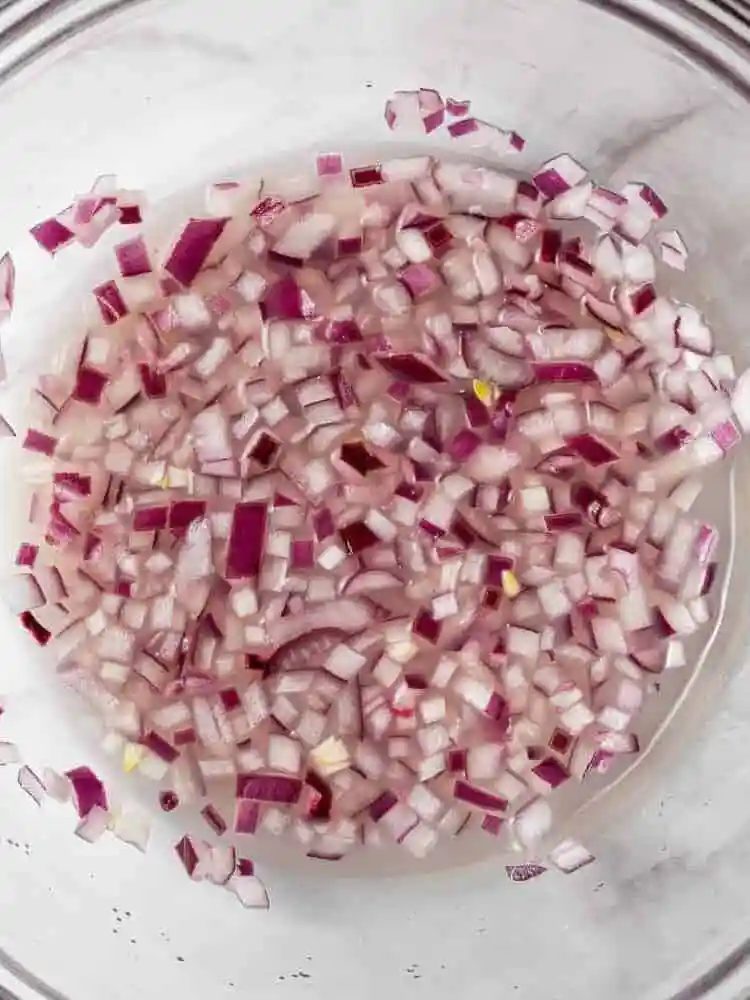 Onions in lime juice in a clear glass bowl.