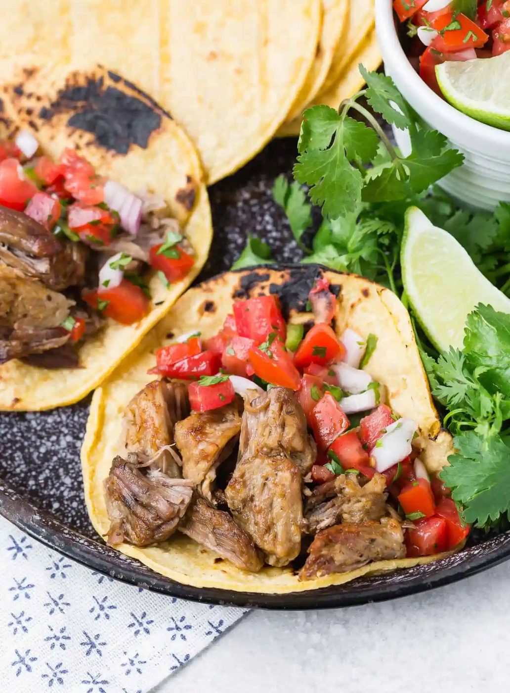 Instant pot carnitas on corn tortillas with pico de gallo, garnished with lime and cilantro.