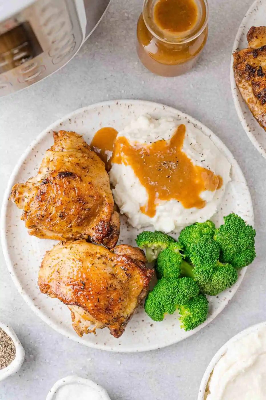 Overhead view of cooked chicken thighs on a plate with broccoli, mashed potatoes, gravy.