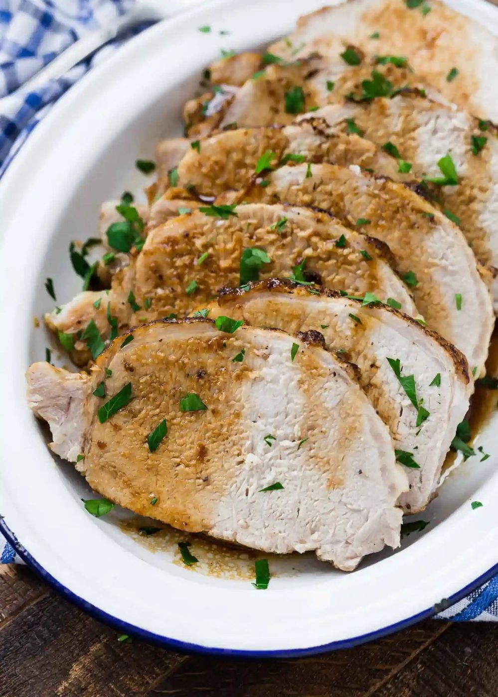 Sliced roast pork with herbs on a white platter, accompanied by a checkered napkin.