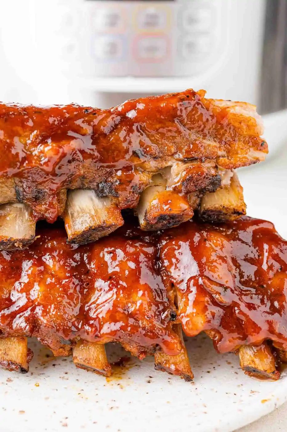 Instant pot ribs stacked in front of a pressure cooker.