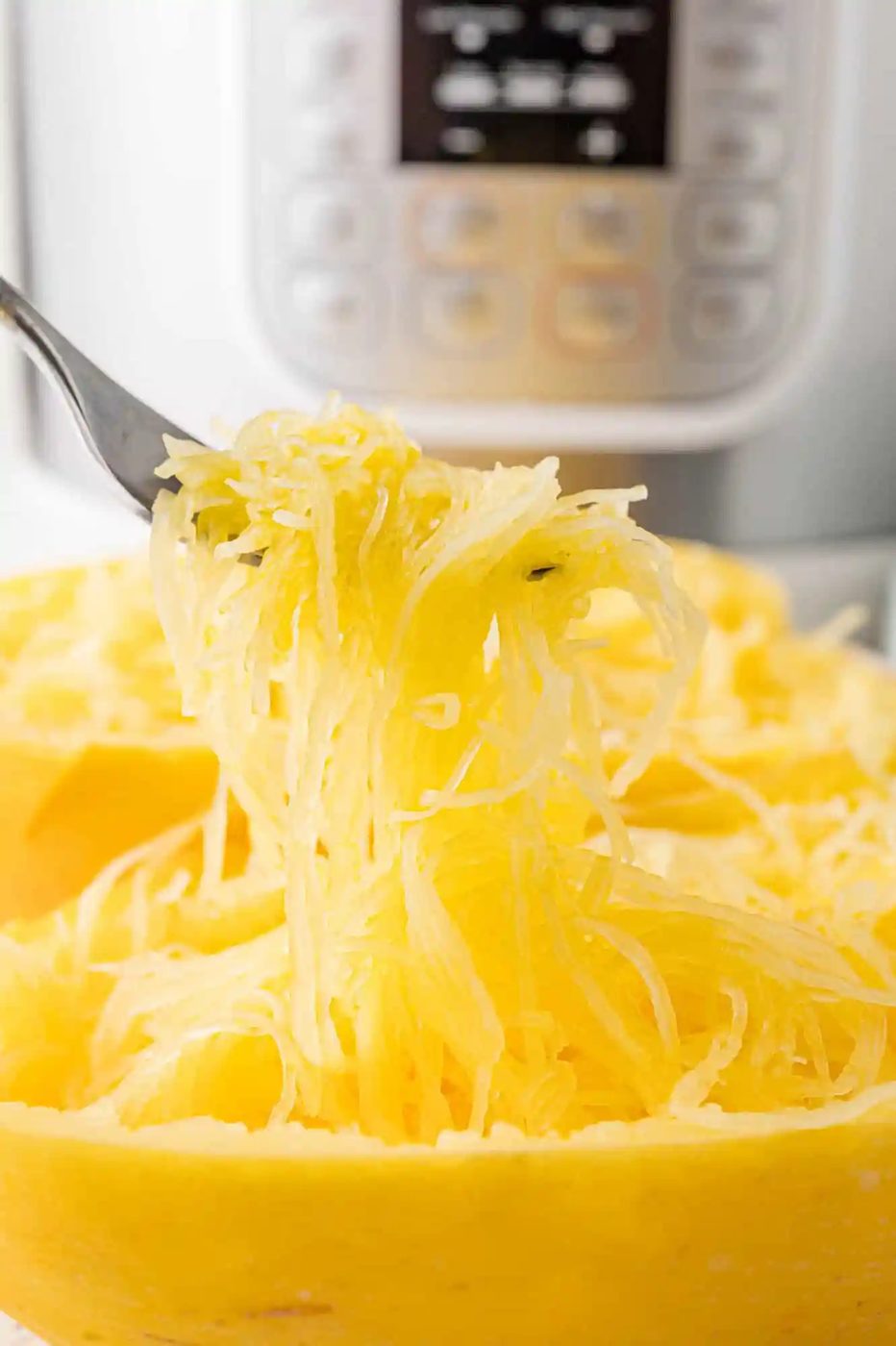 Spaghetti squash strands being lifted out of peel with a fork, held in front of an Instant Pot.