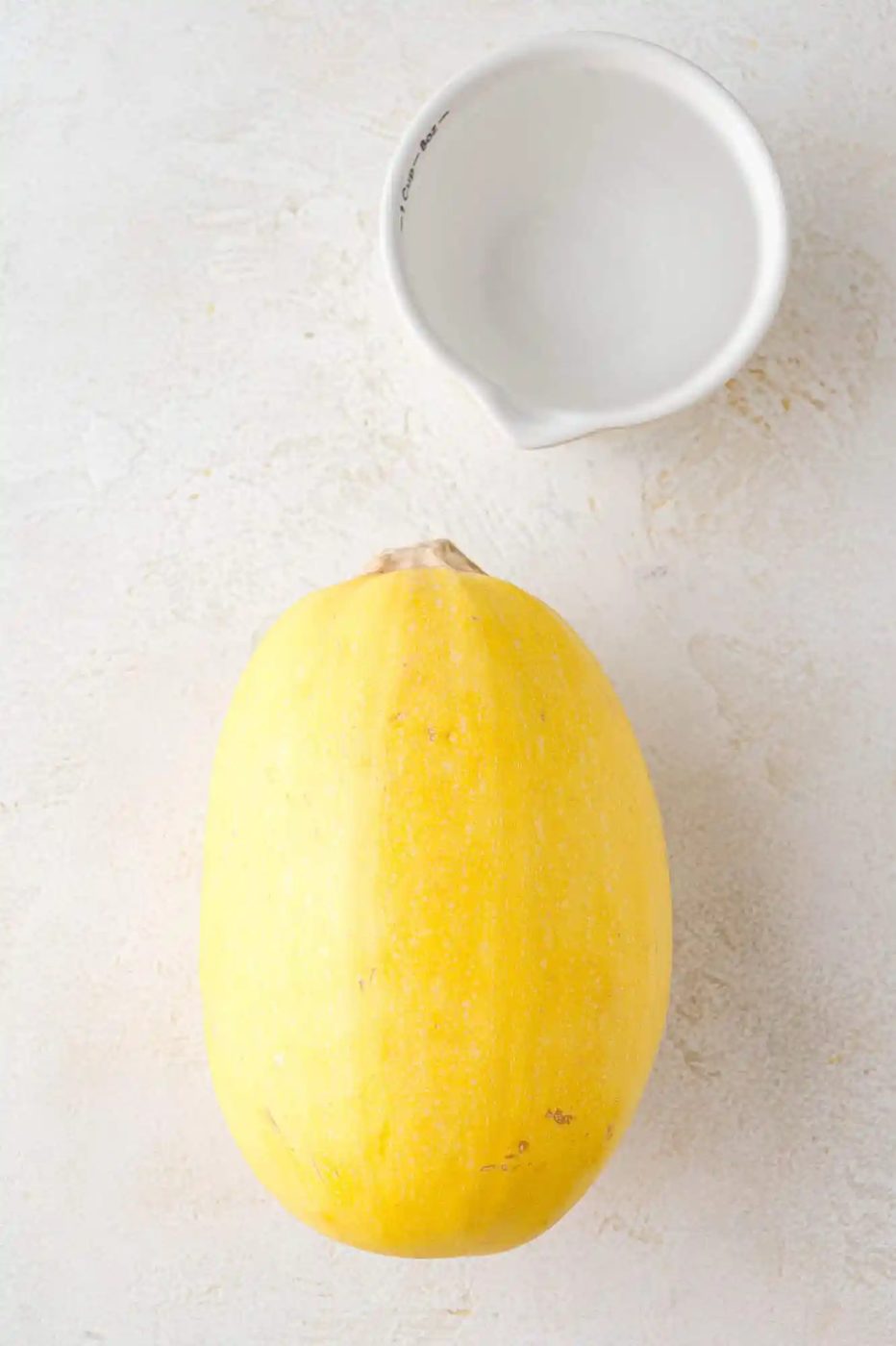 Spaghetti squash and small cup of water, on a white surface.