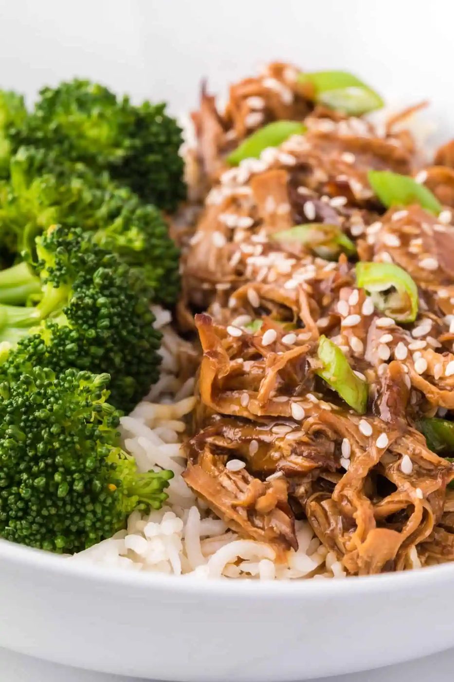 Close up of teriyaki chicken served next to broccoli in a bowl of white rice.