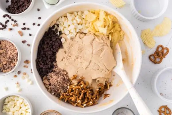 Add-ins for kitchen sink cookies added to cookie dough in a mixing bowl.
