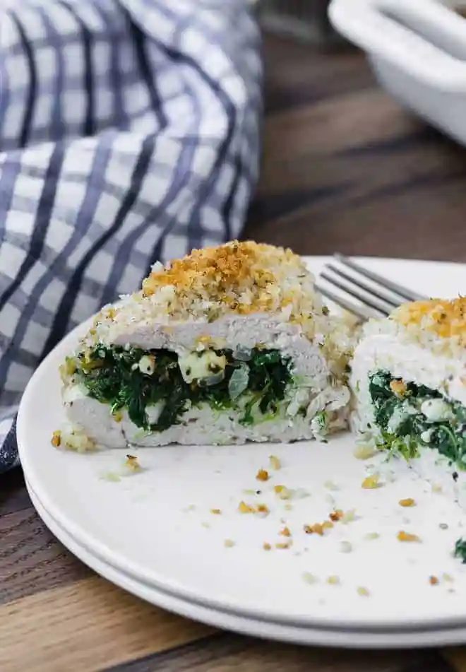 A baked chicken breast on a white plate, cut open to show a filling of spinach and feta cheese.