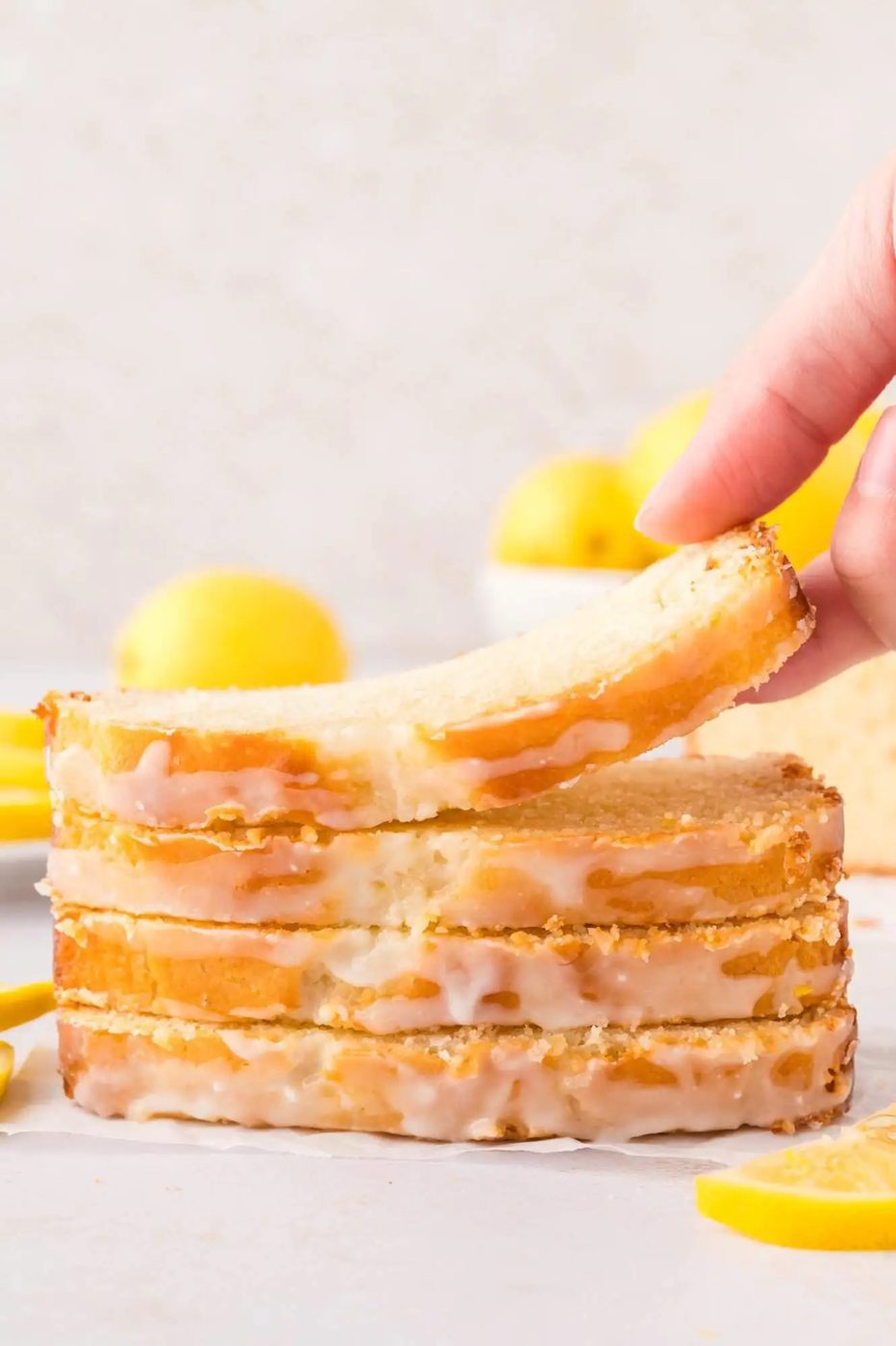 Stack of lemon bread slices, the top slice being lifted by a hand.