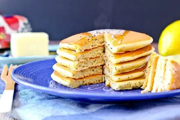 Front view of a stack of lemon poppy seed pancakes with a section cut out.