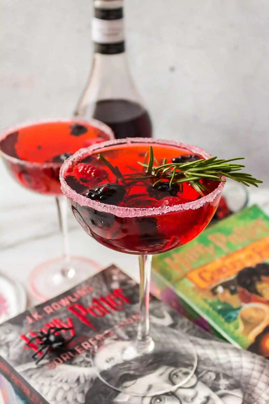 Two bright red cocktails with fruit and rosemary garnishes.