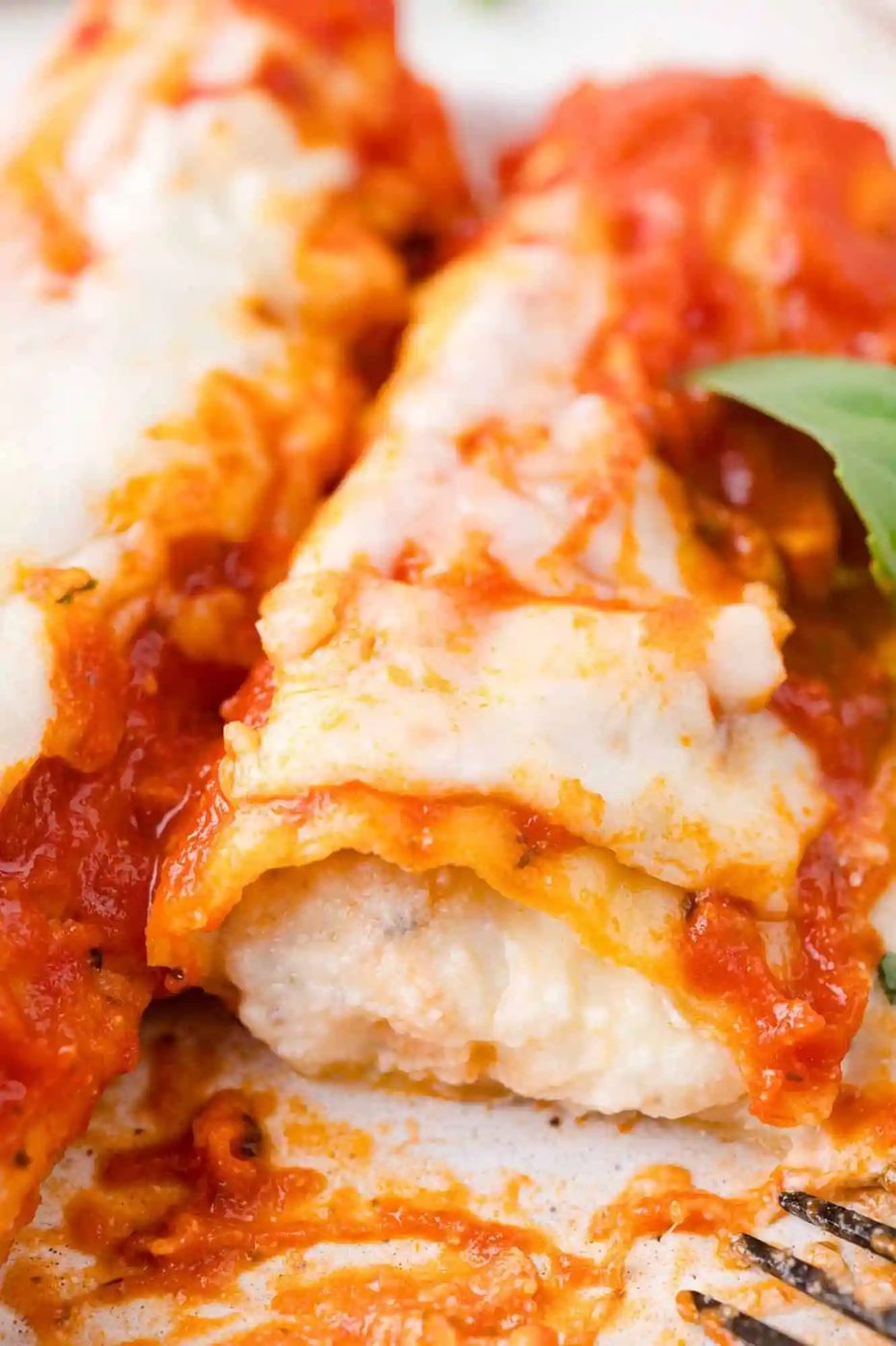 Close-up of manicotti topped with melted cheese and tomato sauce, garnished with a basil leaf.