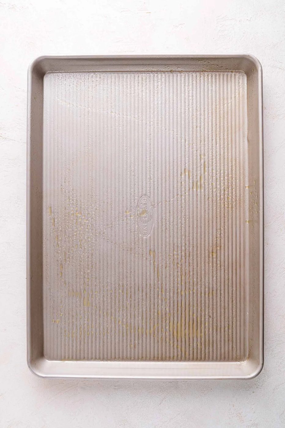 Rectangular metal baking sheet with slight oil, resting on a light textured surface.