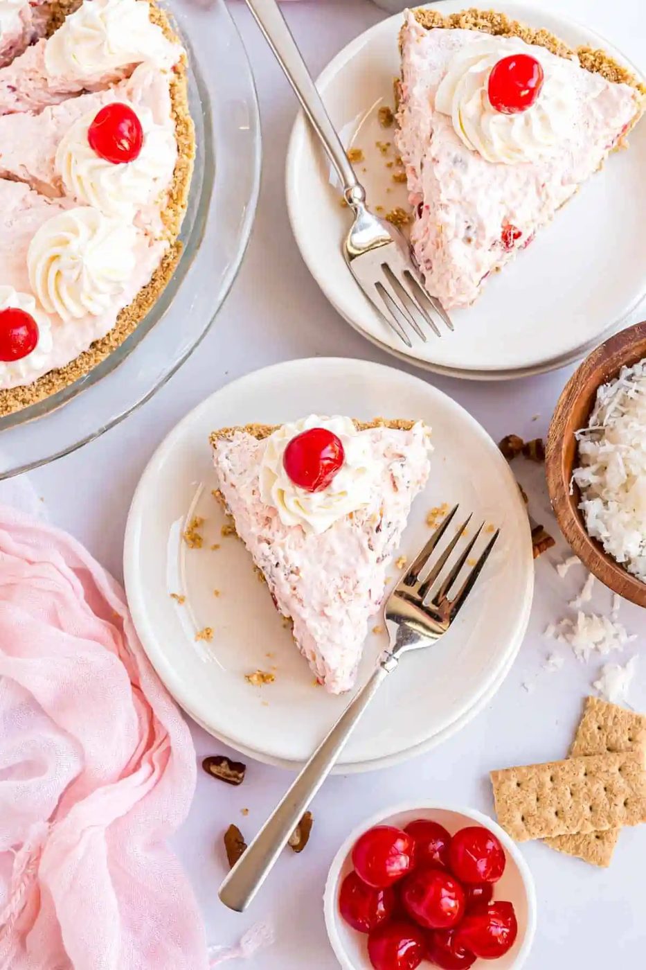 Overhead view of a whipped cream and maraschino cherry topped pie slice on a white plate.