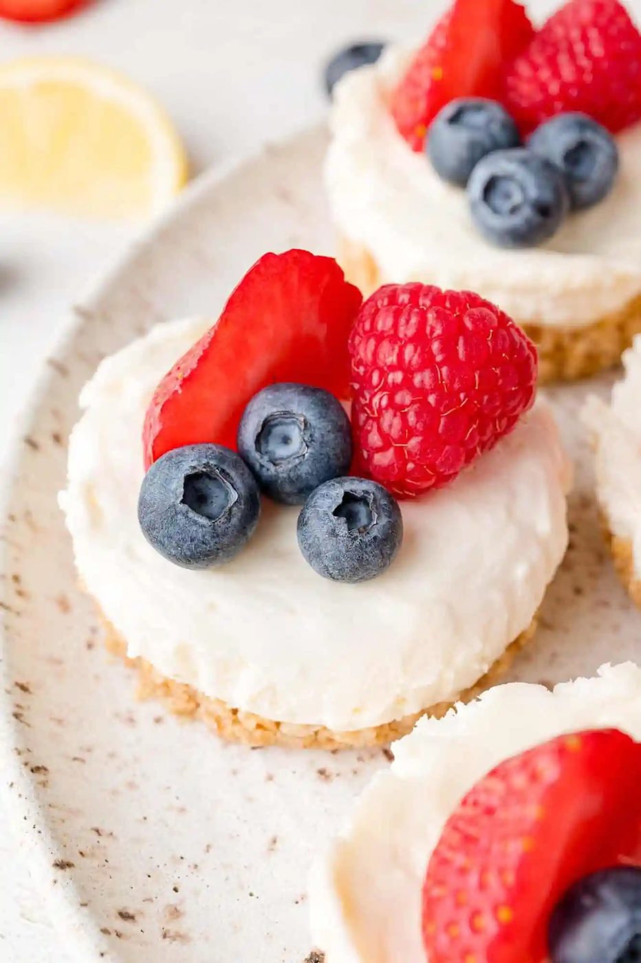 Mini cheesecakes topped with blueberries, raspberries, and strawberry slices on a plate.