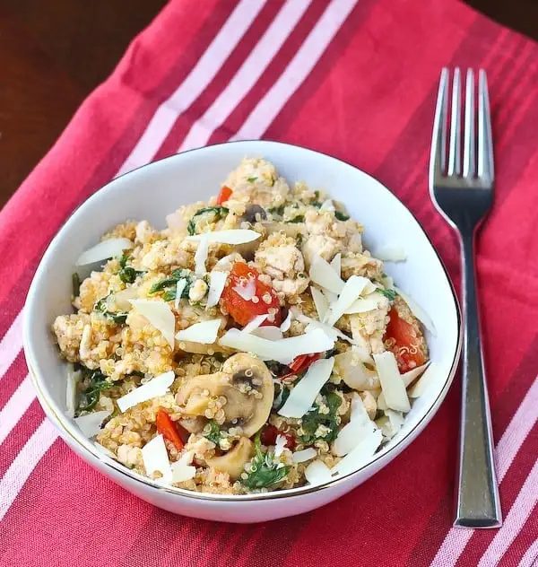 Quinoa recipe in round white bowl on striped red cloth.