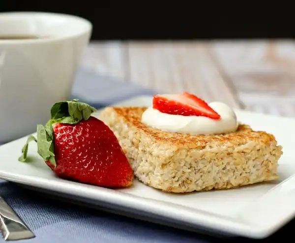 Front view of a serving of oatmeal on white plate, with coffee cup in background.
