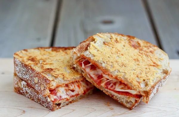 Prepared pizza grilled cheese sandwich cut in half on white surface.