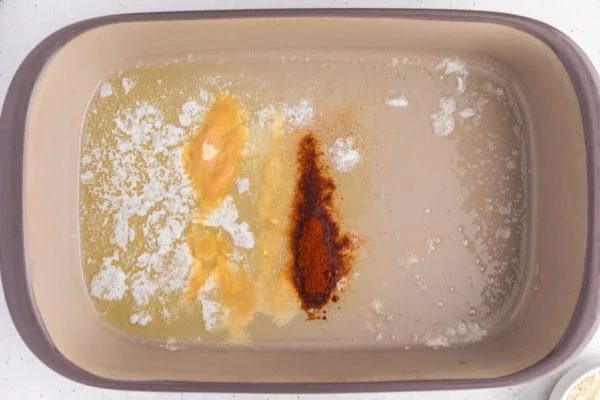 Seasonings added to melted butter in a baking dish.