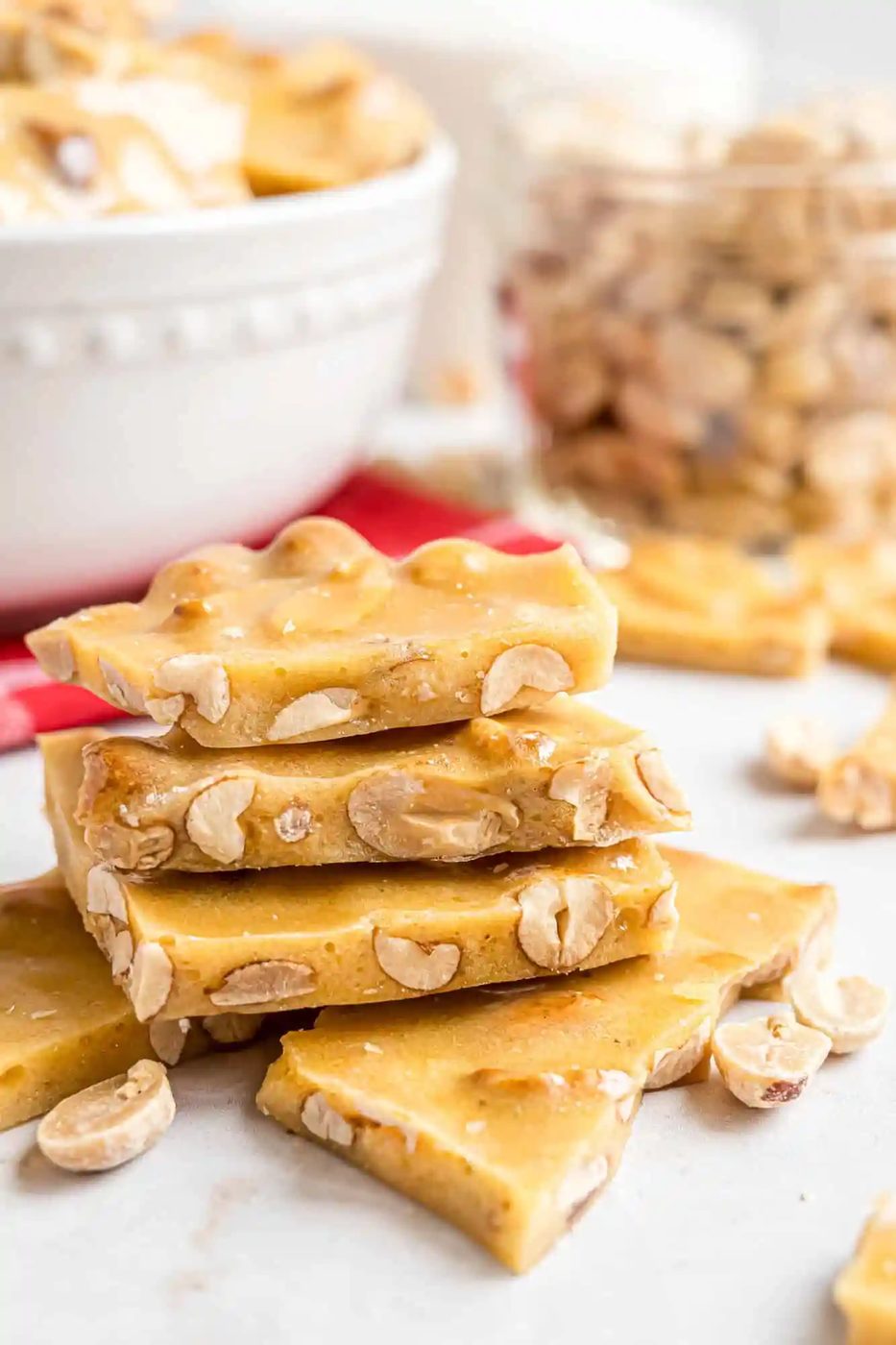 A stack of golden peanut brittle pieces with visible peanuts, set on a white surface.