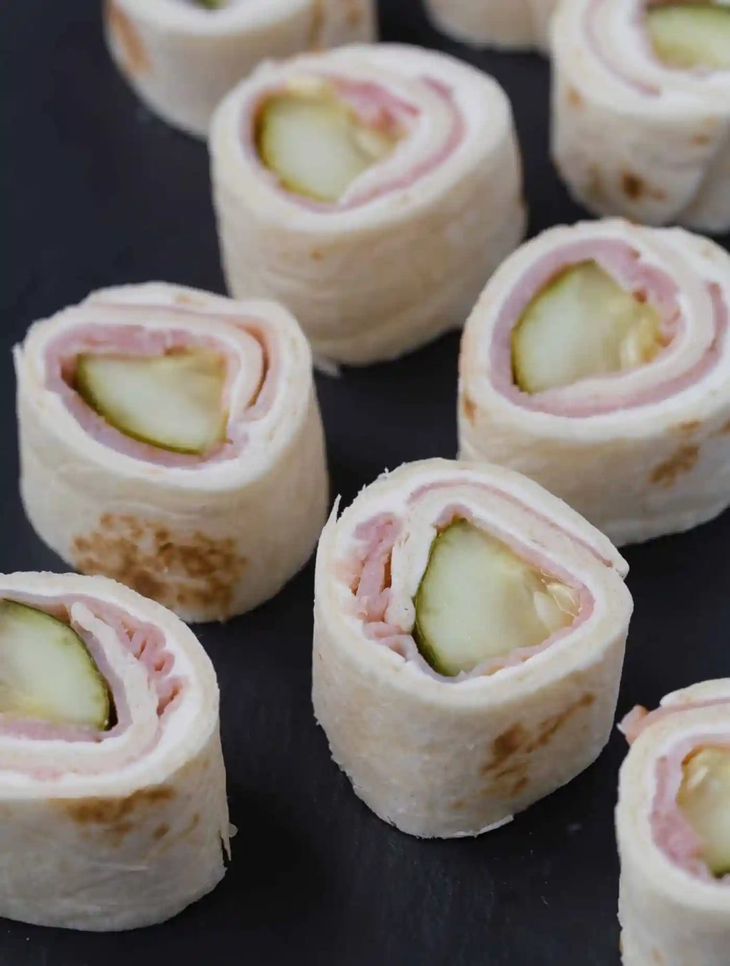 Slices of pickle roll ups on a black background.