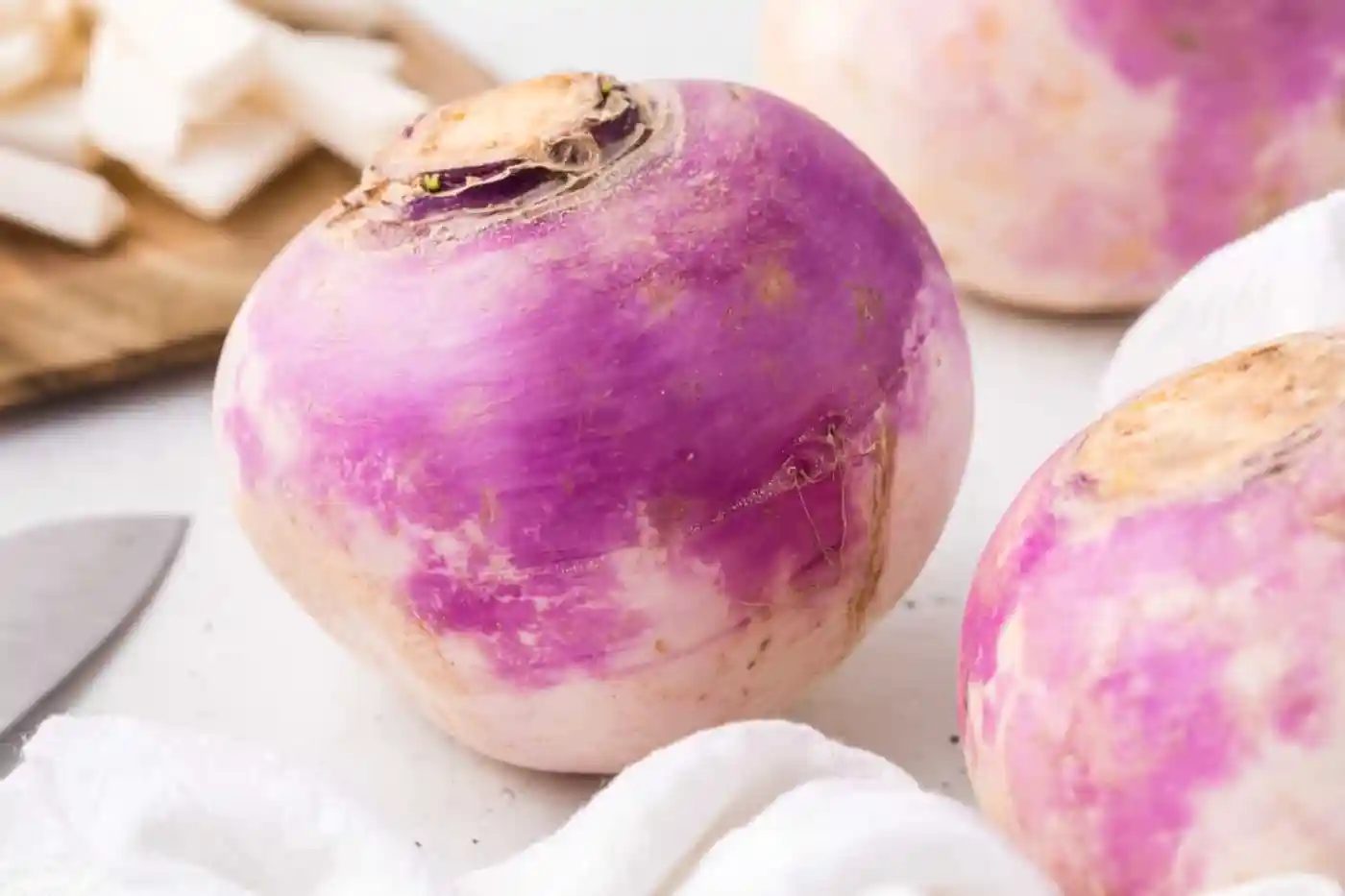 Turnips, with a knife partially visible, and some sliced turnips in background.