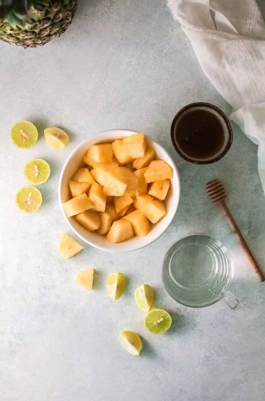 Pineapple, lime, water, and honey on a light grey surface.