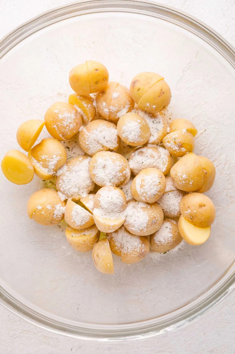 Small yellow potatoes in a glass bowl, some halved, sprinkled with a layer of ranch seasoning.