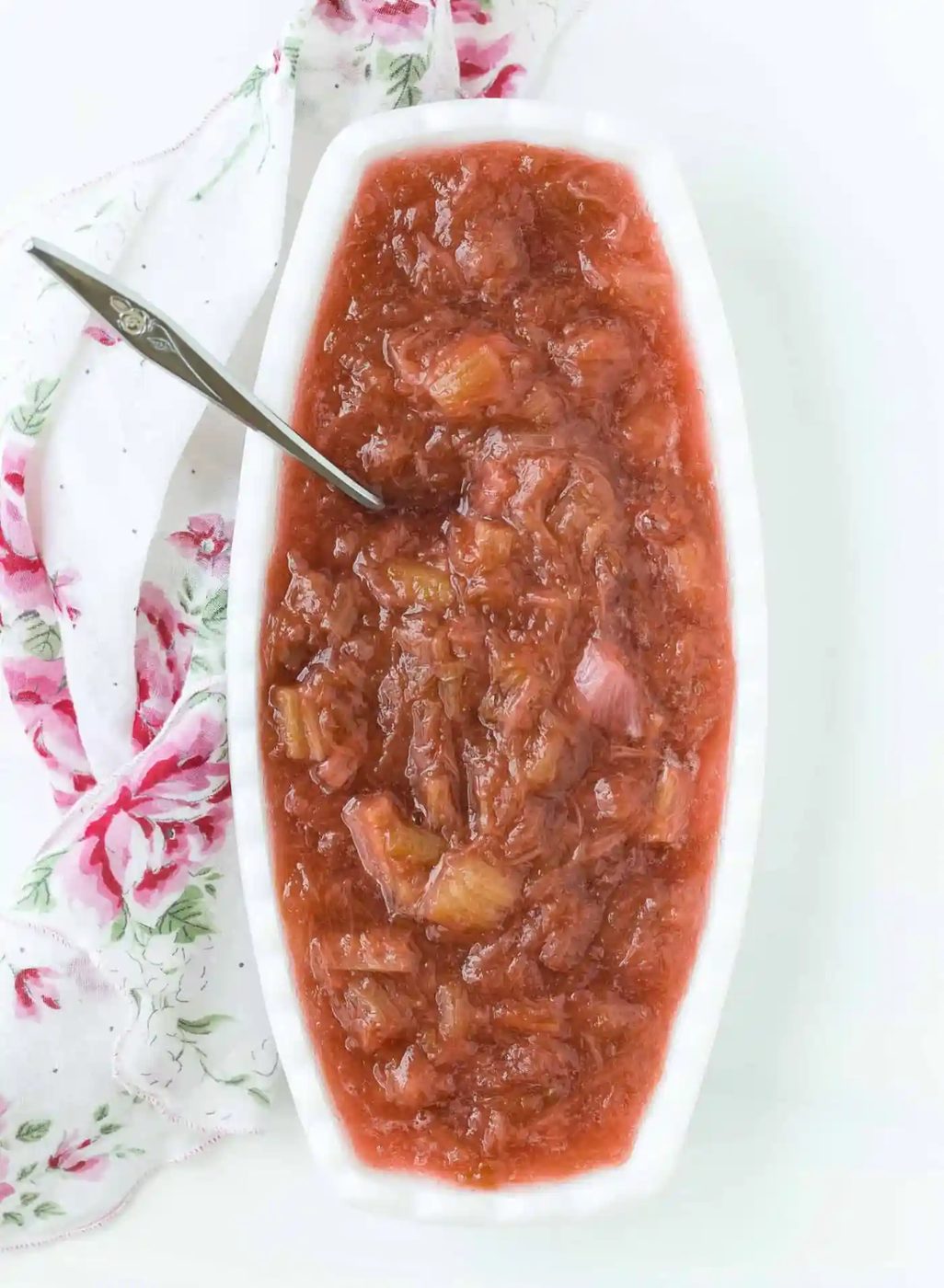 Rhubarb sauce in an oval shaped white bowl, with a silver spoon.