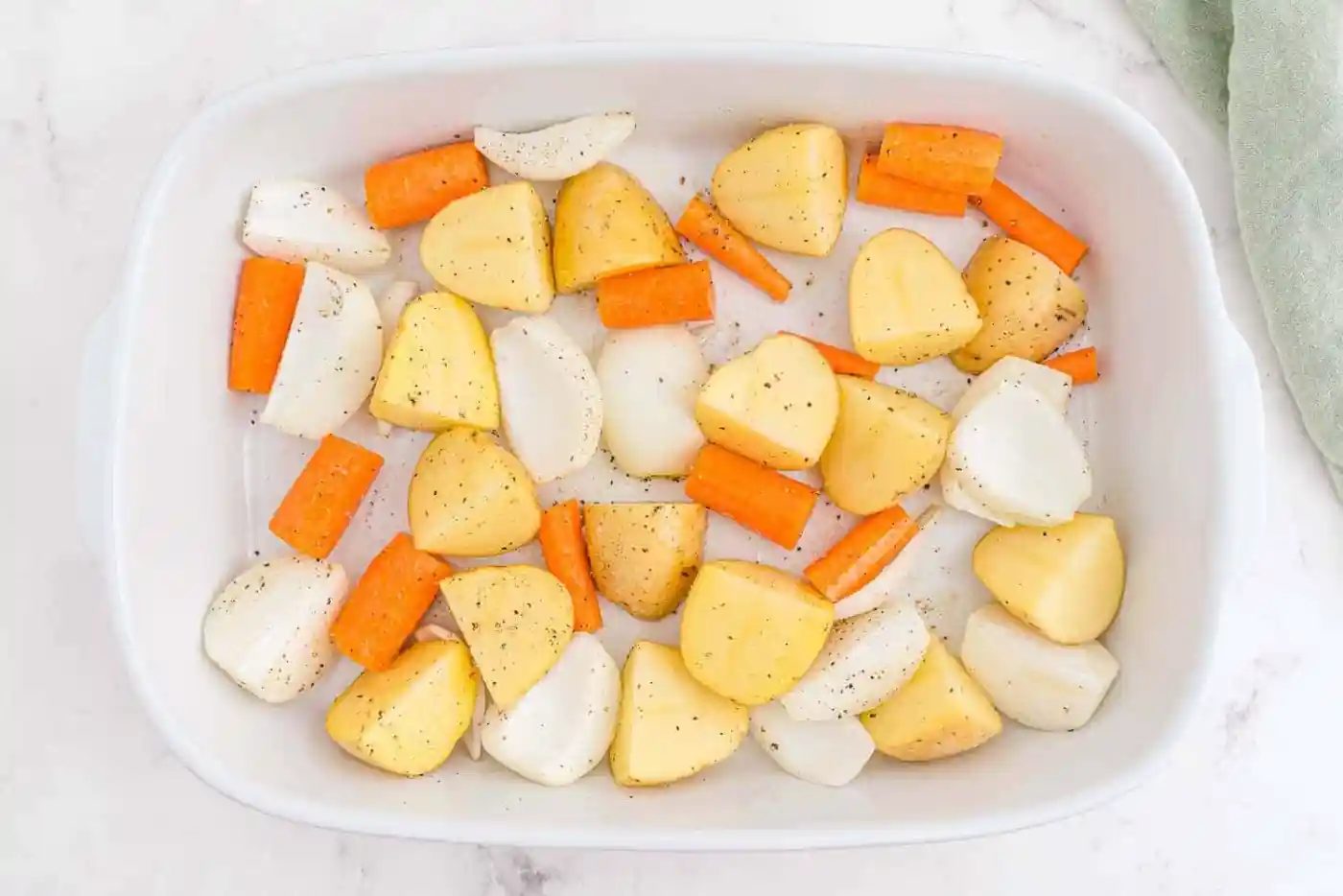 Potatoes, onions, and carrots in a white baking dish.