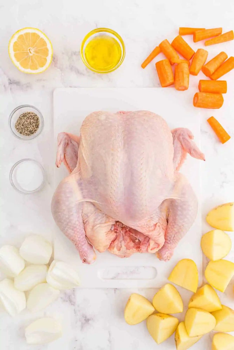 Overhead view of ingredients needed, a chicken, carrots, potatoes, onions and more.