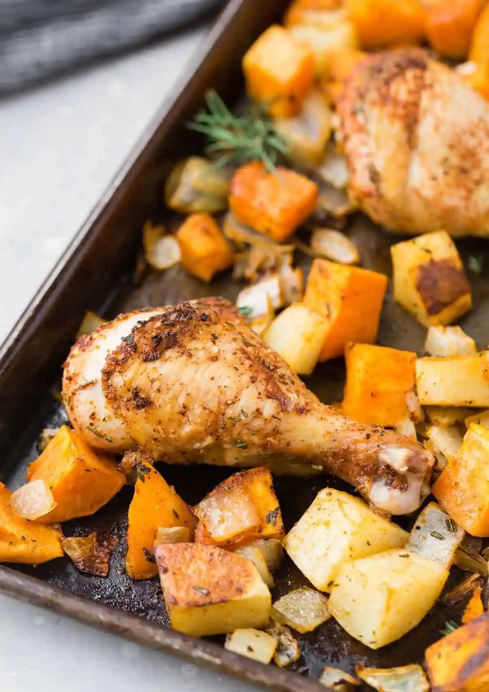 Roasted chicken drumsticks on a pan with potatoes and onions.
