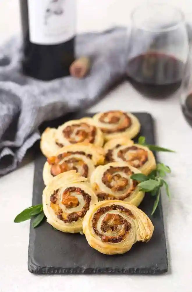 Puff pastry pinwheels on a slate board with fresh sage. Red wine in background.