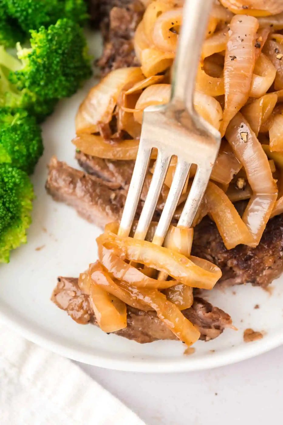 Sautéed onions on top of a steak on a plate with broccoli.