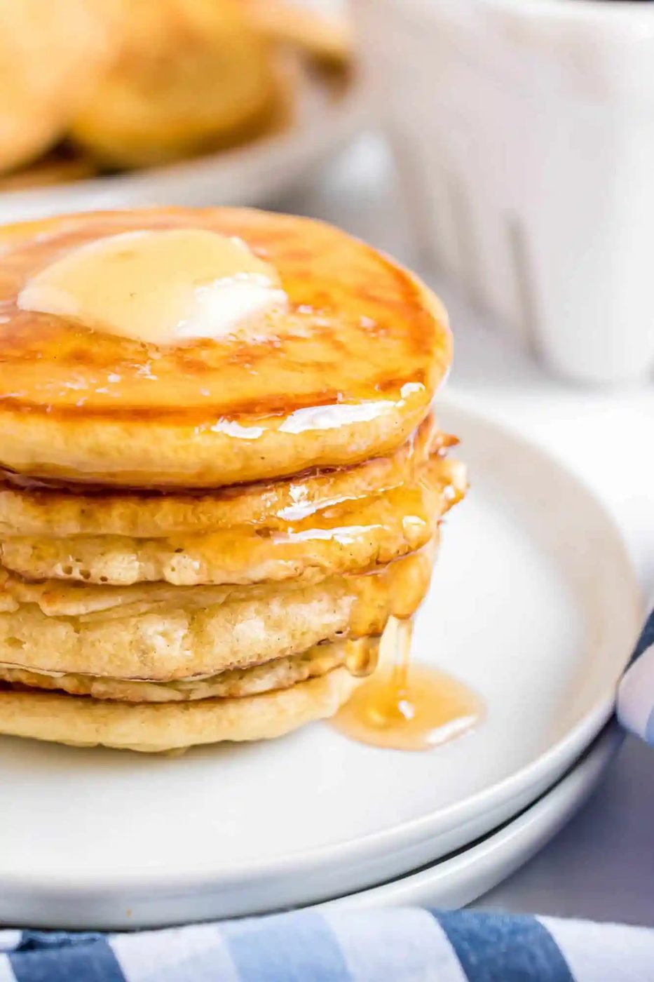 A stack of silver dollar pancakes with a pat of butter on top, drizzled with syrup, on a white plate.