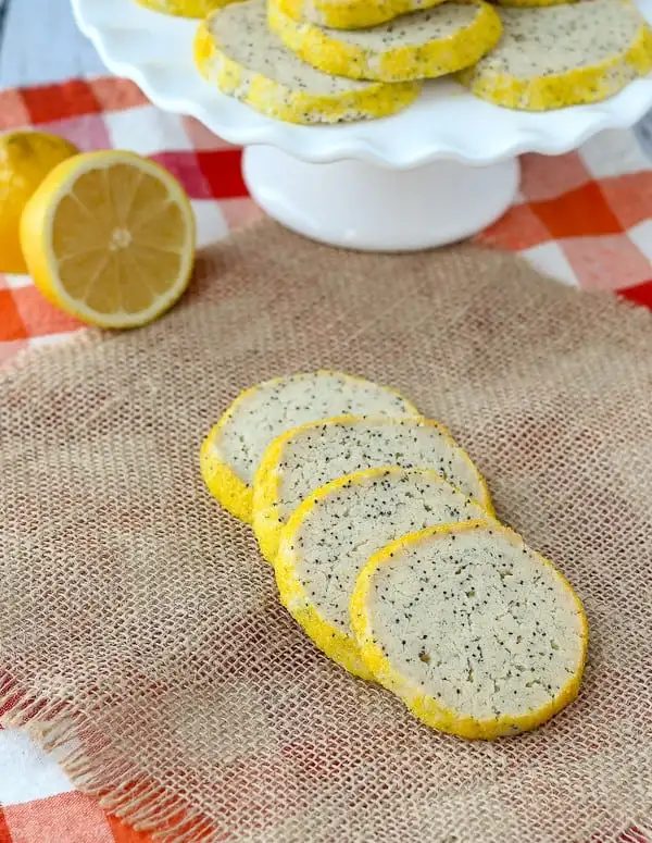 Overhead of four cookies layered on burlap cloth with cut lemon and pedestal platter in background.