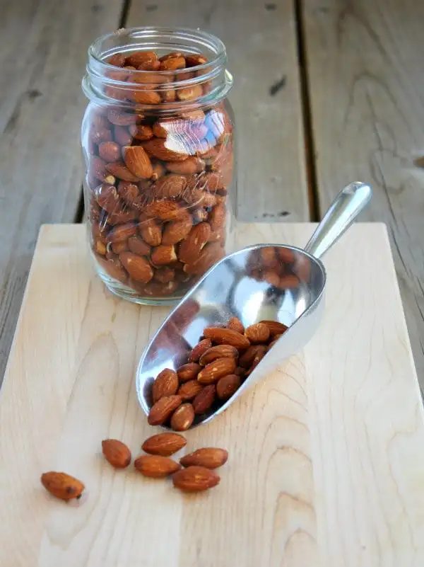 Almonds on a scoop and in a jar on a wooden surface.