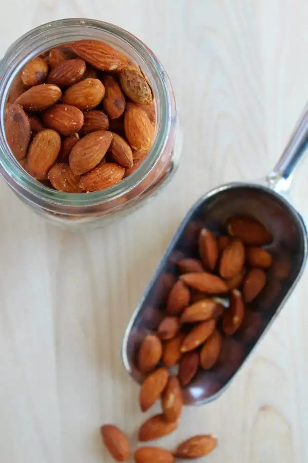Almonds on a scoop and in a jar on a wooden surface.