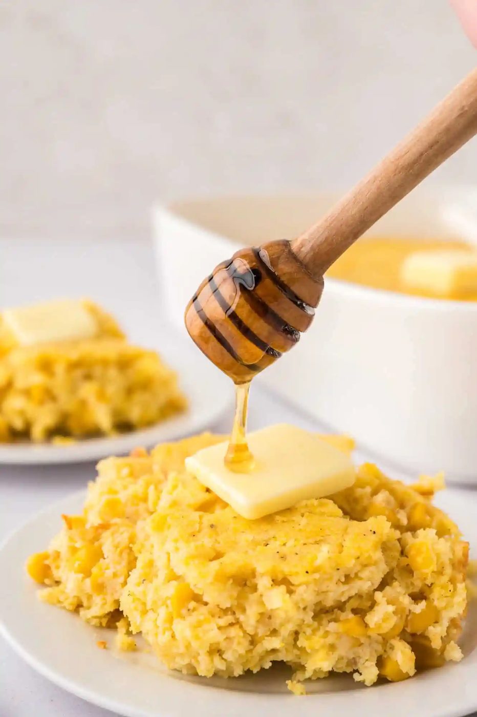 Honey being drizzled on a butter-topped piece of corn spoon bread.