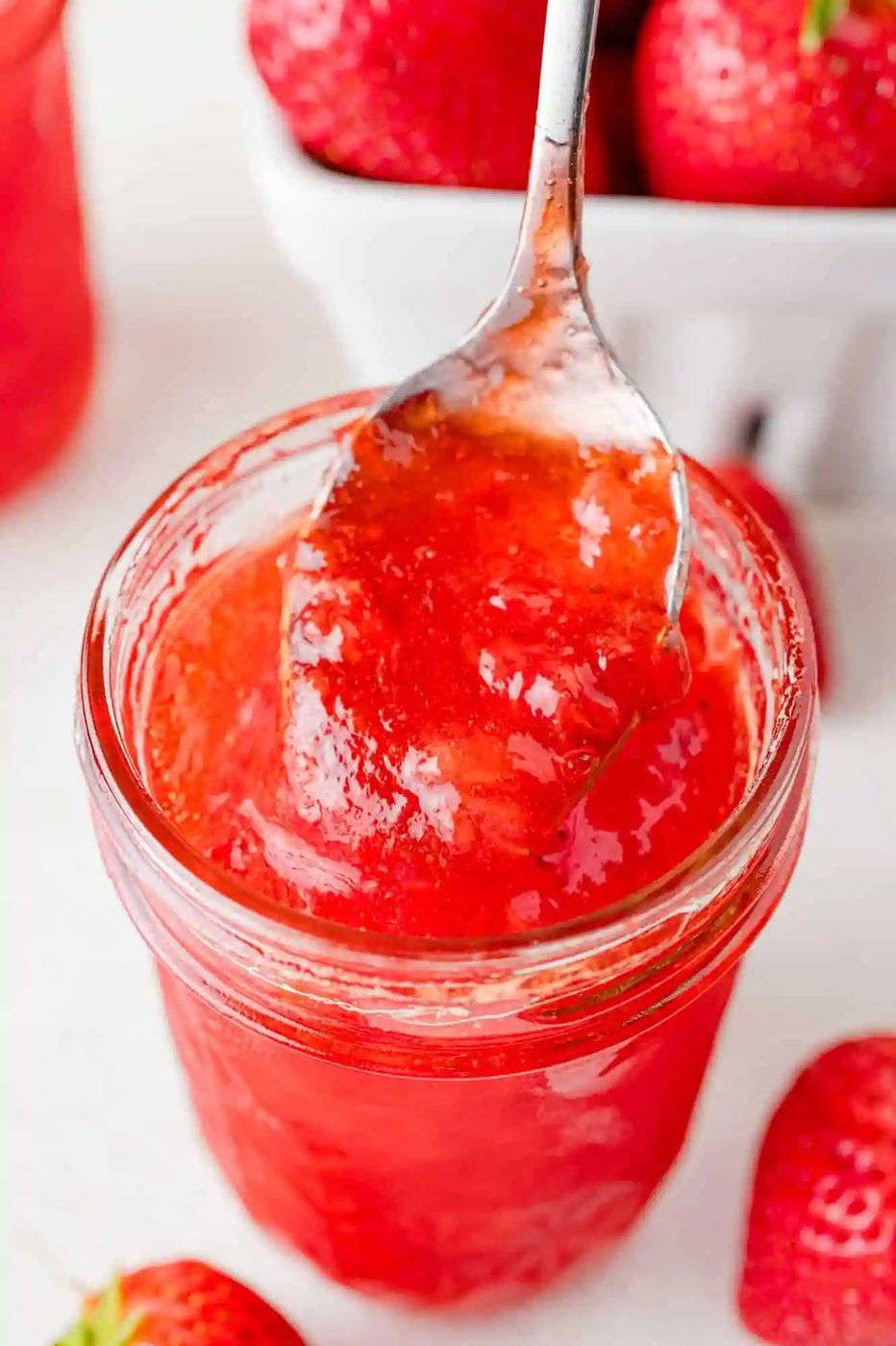 Strawberry jam on a spoon being scooped out of a jar.