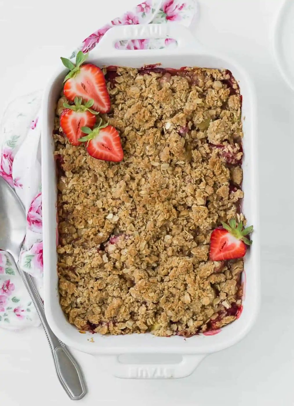 Overhead view of a white baking dish full of cooked strawberries and rhubarb, topped with fresh strawberry halves.