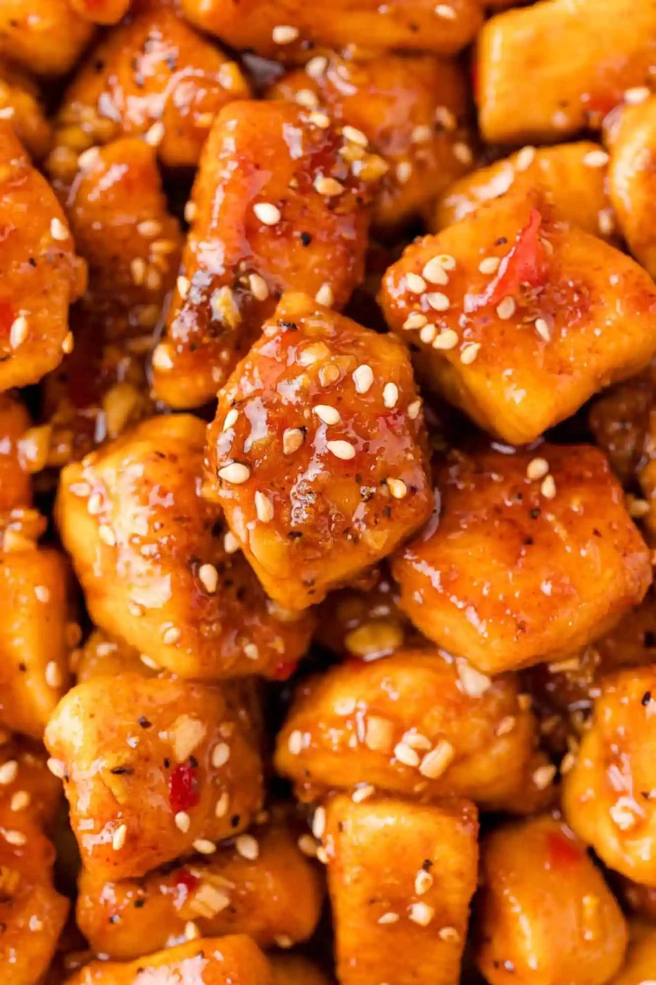 Close-up of cubed chicken coated in a glossy sauce with sesame seeds sprinkled on top.