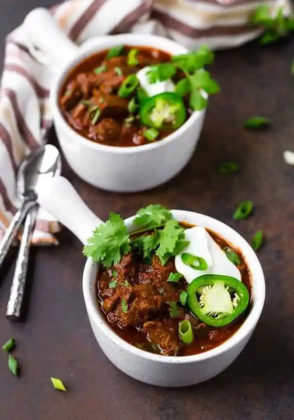Two bowls of chili, garnished, with spoons and napkins nearby.