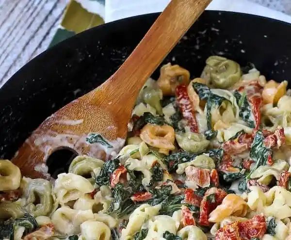 Partial closeup image of tortellini in skillet with wooden spoon.