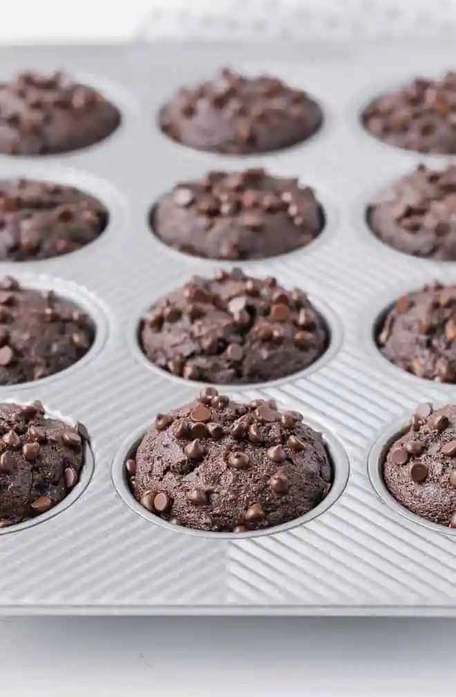 A muffin pan full of whole wheat chocolate muffins, sprinkled with mini chocolate chips.