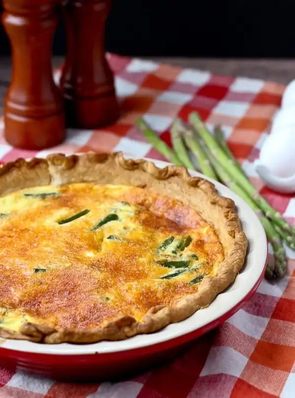 Turkey sausage quiche in a red pie dish with asparagus and salt and pepper shakers in the background.