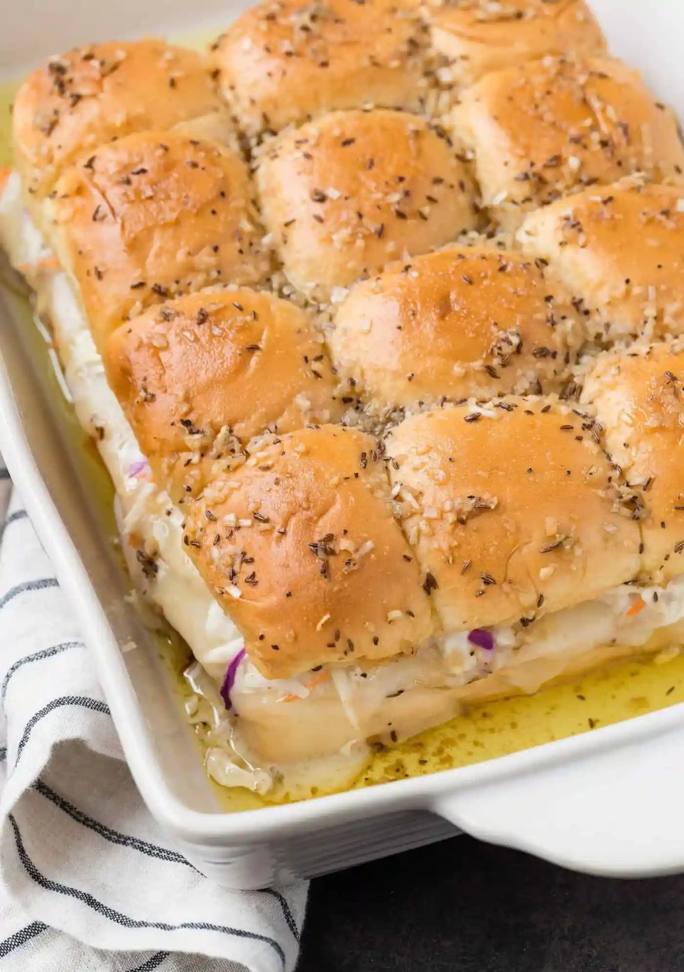 the kitchen Sandwich sliders baked in a white baking dish, topped with caraway seeds.