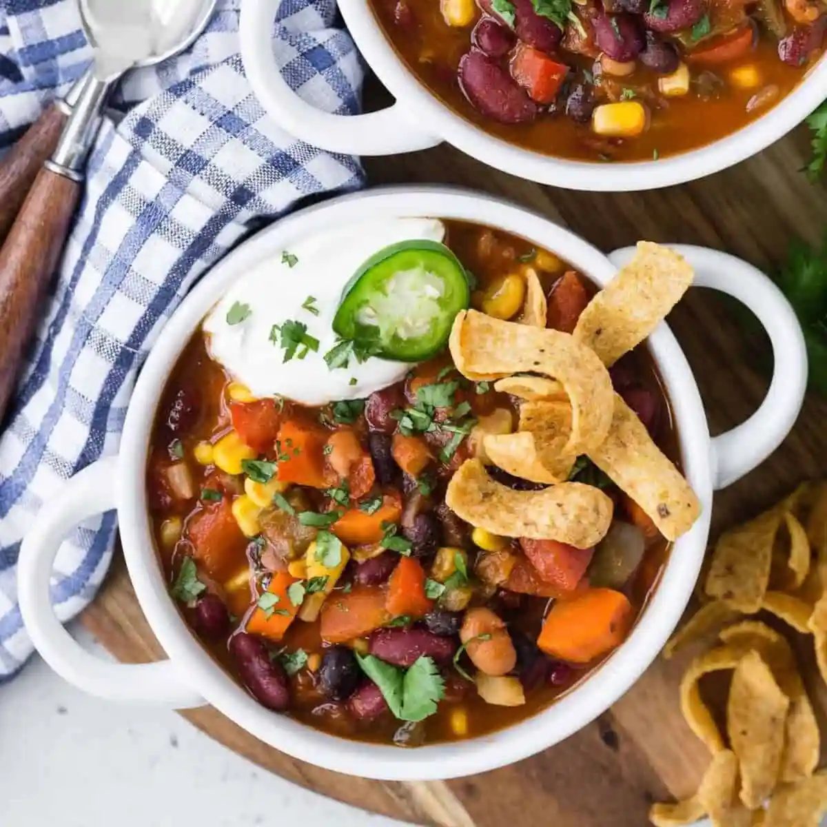Overhead view of chili in a white bowl with fritos, sour cream, jalapeno.